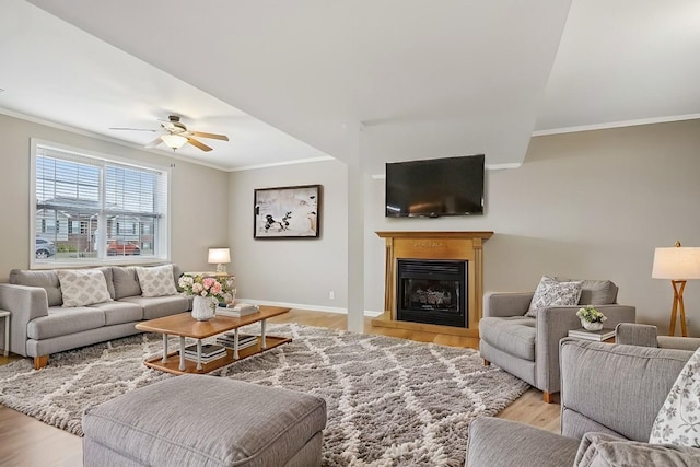 living area with light wood finished floors, a fireplace with raised hearth, ornamental molding, ceiling fan, and baseboards