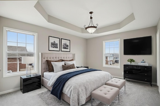 bedroom featuring light carpet, baseboards, multiple windows, and a tray ceiling