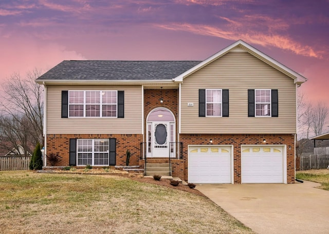 bi-level home featuring driveway, brick siding, a lawn, and an attached garage