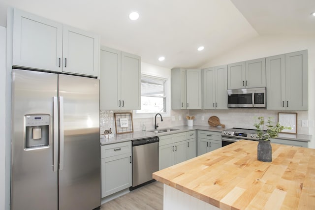 kitchen with butcher block countertops, tasteful backsplash, lofted ceiling, sink, and stainless steel appliances