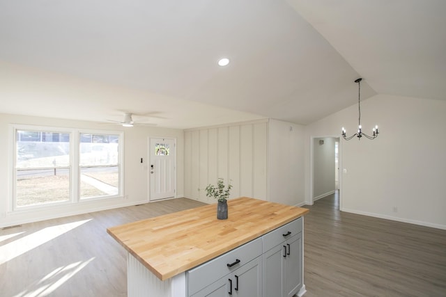 kitchen with ceiling fan with notable chandelier, butcher block counters, wood-type flooring, decorative light fixtures, and vaulted ceiling