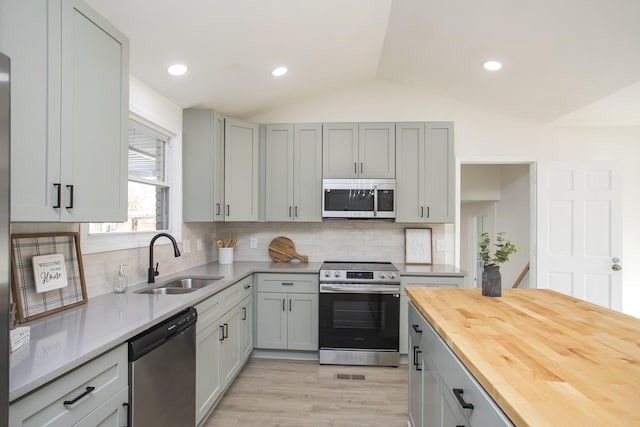 kitchen featuring vaulted ceiling, butcher block countertops, sink, gray cabinetry, and stainless steel appliances