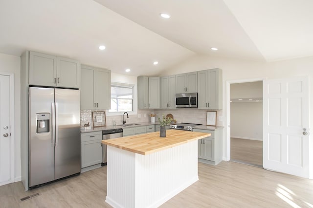 kitchen with butcher block countertops, sink, stainless steel appliances, a center island, and vaulted ceiling