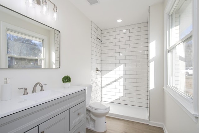 bathroom featuring vanity, wood-type flooring, tiled shower, and toilet