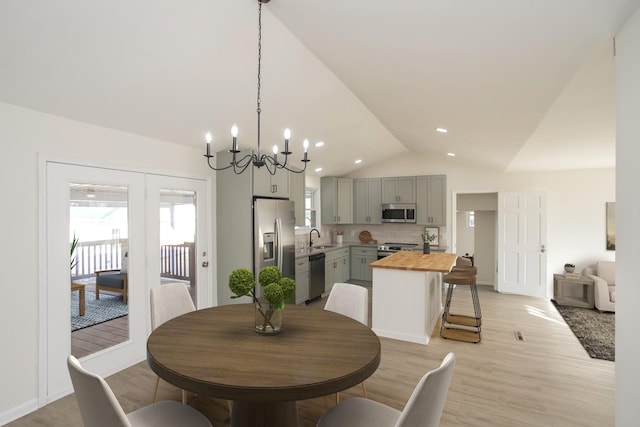 dining area with lofted ceiling, sink, a notable chandelier, and light hardwood / wood-style flooring