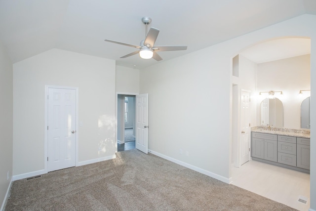 unfurnished bedroom with vaulted ceiling, sink, light colored carpet, ceiling fan, and ensuite bath