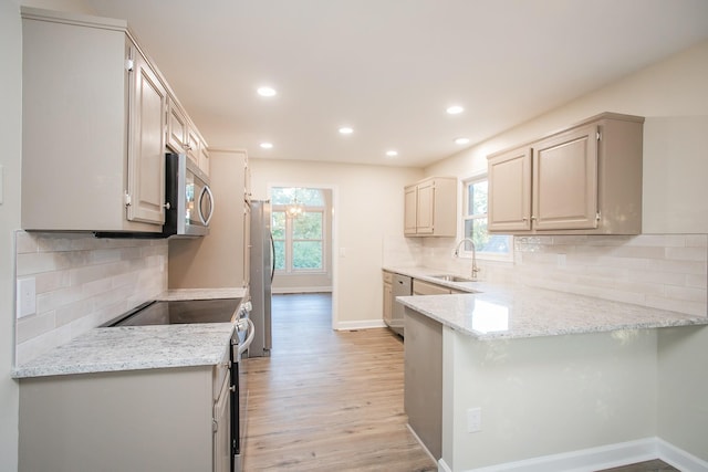 kitchen featuring appliances with stainless steel finishes, sink, kitchen peninsula, light stone countertops, and a healthy amount of sunlight