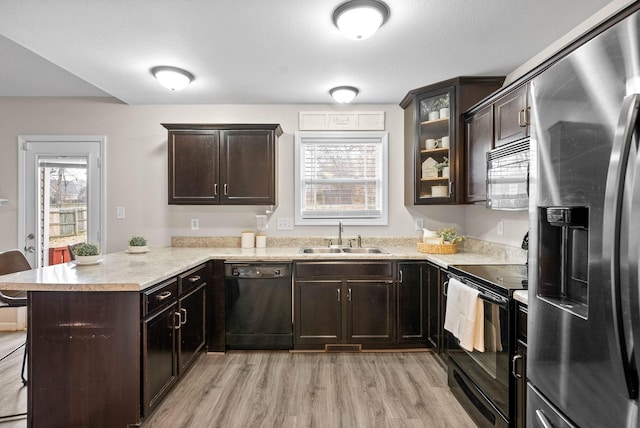 kitchen with sink, dark brown cabinetry, black appliances, kitchen peninsula, and light wood-type flooring