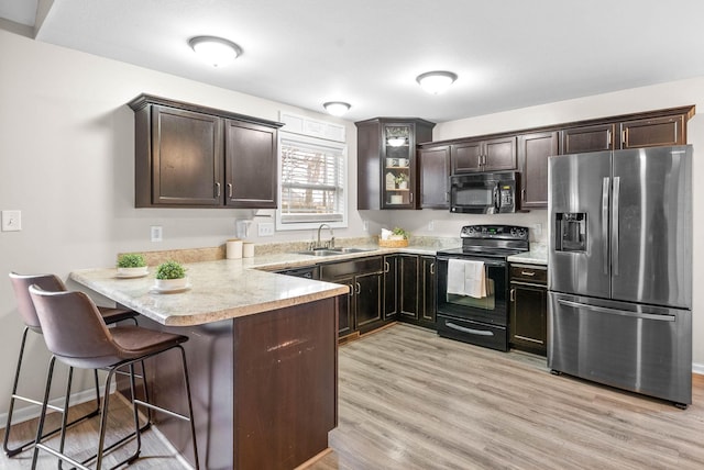 kitchen featuring dark brown cabinets, sink, a breakfast bar, and black appliances