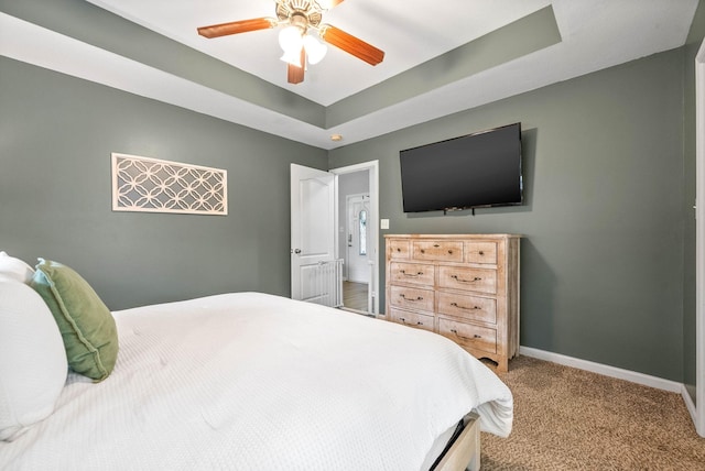 carpeted bedroom with ceiling fan and a tray ceiling