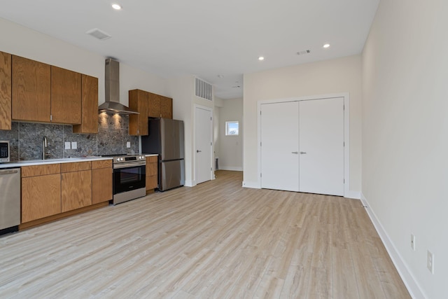 kitchen featuring appliances with stainless steel finishes, tasteful backsplash, sink, light wood-type flooring, and wall chimney exhaust hood