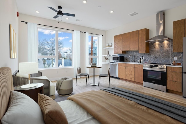 kitchen with appliances with stainless steel finishes, sink, decorative backsplash, wall chimney range hood, and light hardwood / wood-style flooring