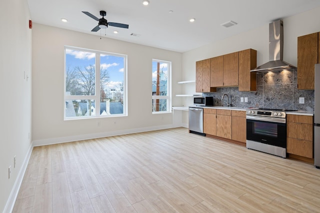 kitchen featuring tasteful backsplash, appliances with stainless steel finishes, wall chimney exhaust hood, and light hardwood / wood-style floors