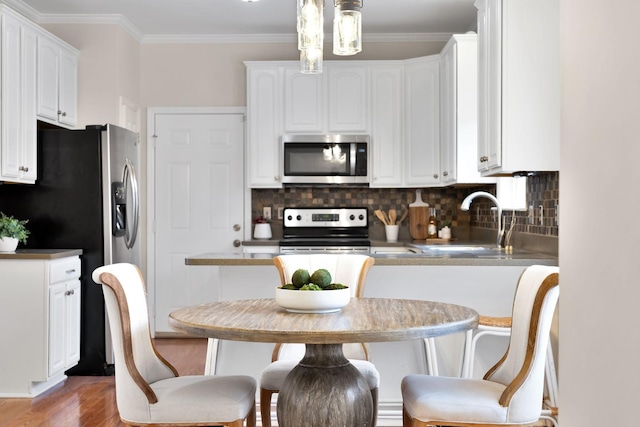 kitchen featuring stainless steel appliances, crown molding, hanging light fixtures, and white cabinets