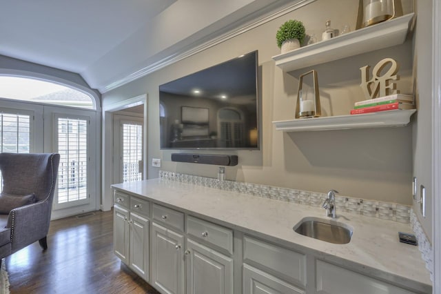 kitchen with dark wood-style flooring, white cabinets, vaulted ceiling, a sink, and light stone countertops