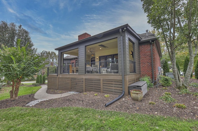 exterior space with a chimney, a ceiling fan, and brick siding