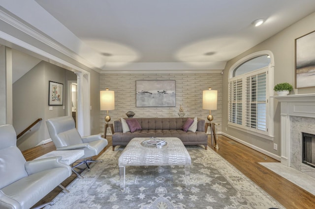 living room with hardwood / wood-style flooring, brick wall, a high end fireplace, and decorative columns