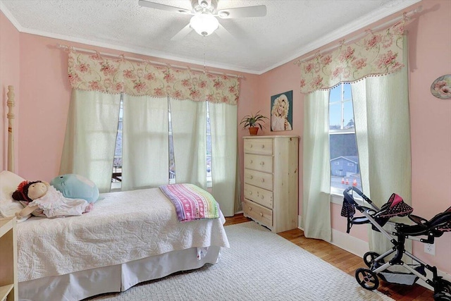 bedroom with ceiling fan, ornamental molding, wood-type flooring, and a textured ceiling