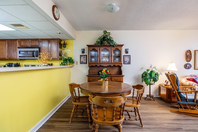 dining space with a paneled ceiling, dark hardwood / wood-style floors, and a textured ceiling