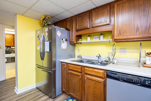 kitchen with stainless steel appliances, sink, light hardwood / wood-style flooring, and a drop ceiling