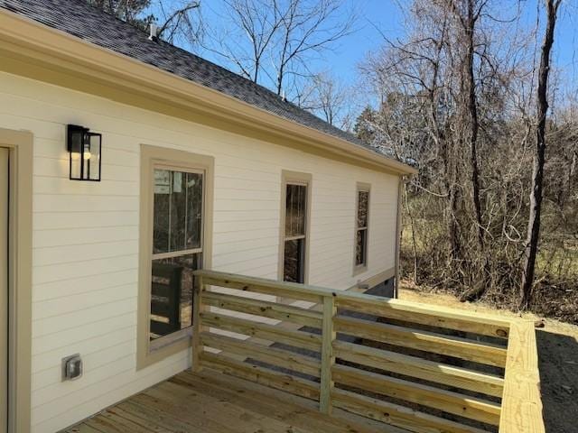 view of exterior entry with roof with shingles and a deck