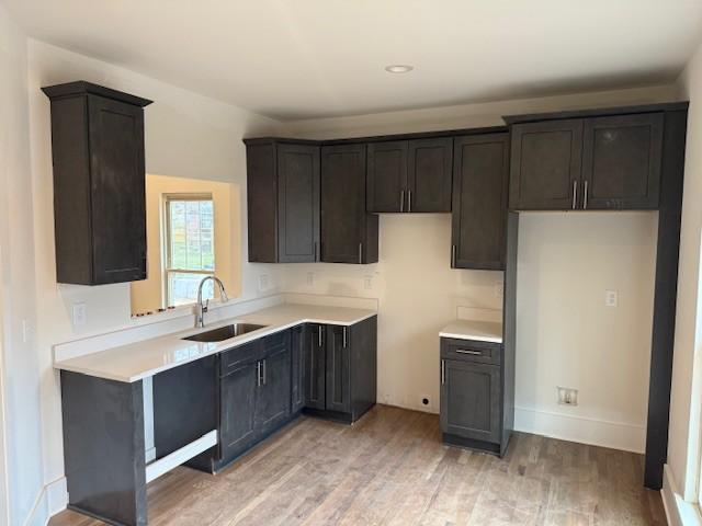 kitchen featuring a sink, baseboards, light wood-style floors, and light countertops