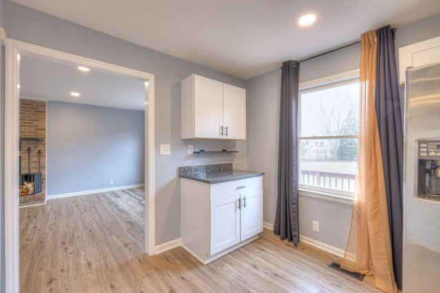 kitchen featuring white cabinetry, dark stone counters, a brick fireplace, and light wood-type flooring