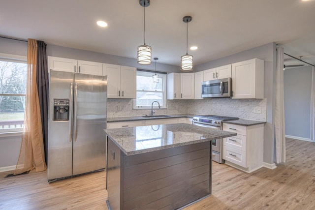 kitchen with sink, white cabinetry, a center island, appliances with stainless steel finishes, and light stone countertops