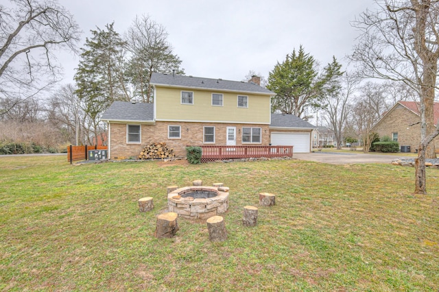 rear view of property featuring a garage, a yard, a deck, and a fire pit