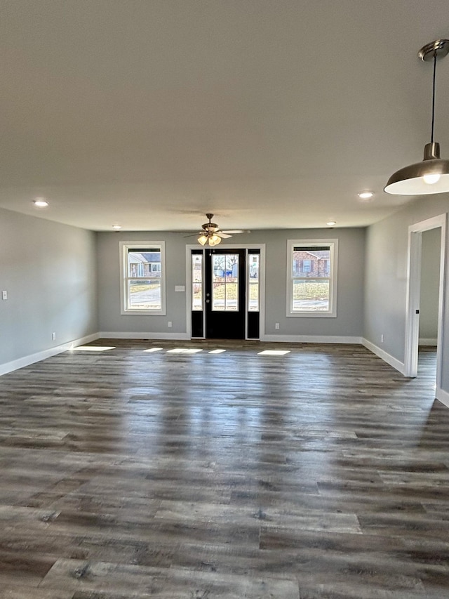 unfurnished living room featuring dark wood-type flooring, ceiling fan, and a wealth of natural light