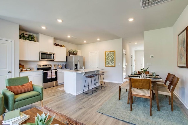 kitchen with a breakfast bar, light wood-type flooring, appliances with stainless steel finishes, an island with sink, and white cabinets