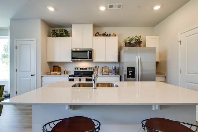 kitchen with white cabinetry, sink, stainless steel appliances, and an island with sink