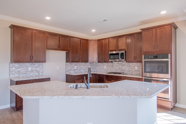 kitchen featuring sink, light stone countertops, appliances with stainless steel finishes, and a center island with sink