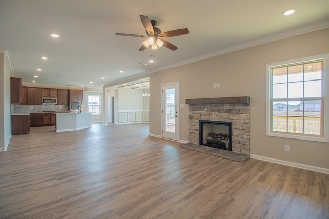 unfurnished living room with crown molding, ceiling fan, a stone fireplace, and light hardwood / wood-style flooring