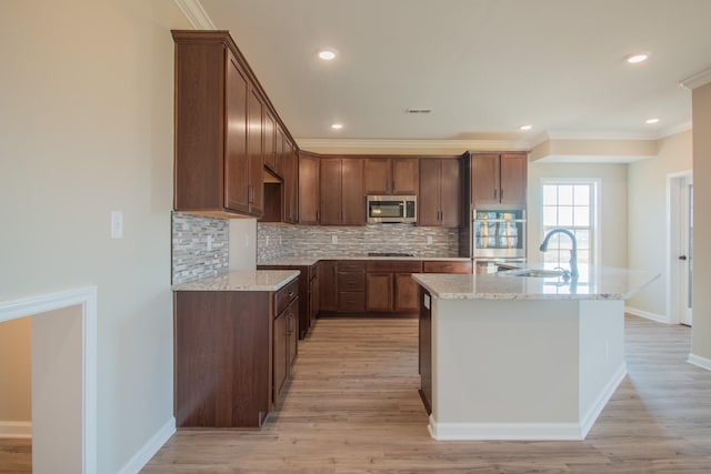 kitchen featuring sink, appliances with stainless steel finishes, tasteful backsplash, light stone countertops, and a center island with sink