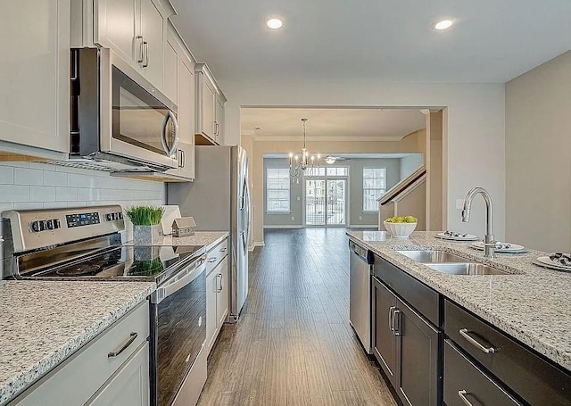 kitchen featuring sink, appliances with stainless steel finishes, pendant lighting, light stone countertops, and backsplash