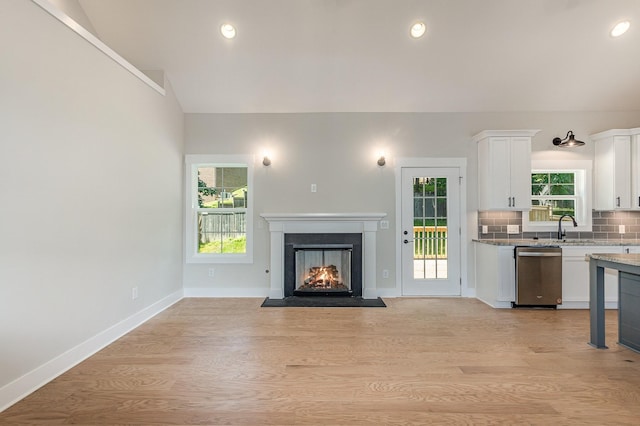 unfurnished living room with lofted ceiling, sink, and light wood-type flooring