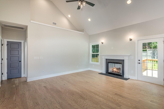 unfurnished living room with a wealth of natural light, visible vents, a lit fireplace, and wood finished floors