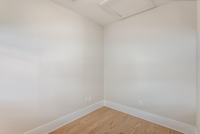 empty room with attic access, light wood-style flooring, and baseboards