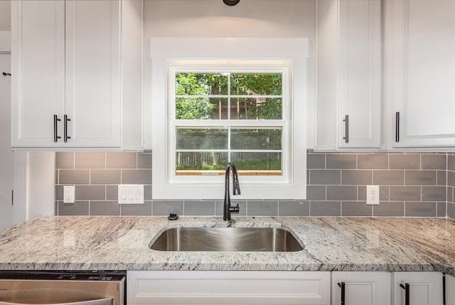 kitchen featuring decorative backsplash, white cabinetry, a sink, and stainless steel dishwasher