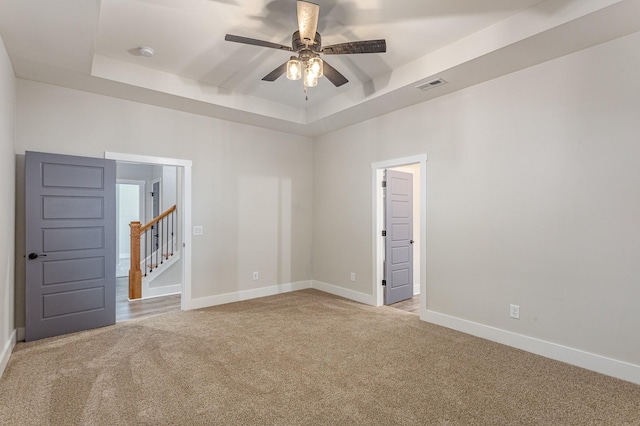 spare room with ceiling fan, a tray ceiling, and light carpet