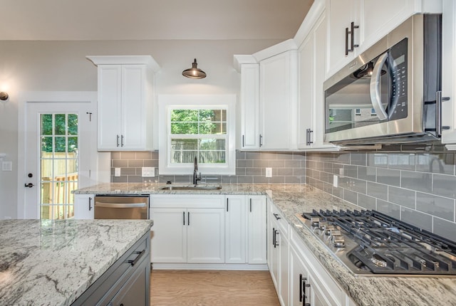 kitchen with sink, light stone counters, appliances with stainless steel finishes, a wealth of natural light, and white cabinets