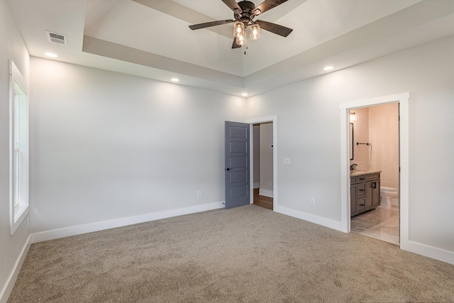 unfurnished bedroom featuring a raised ceiling, connected bathroom, and light colored carpet