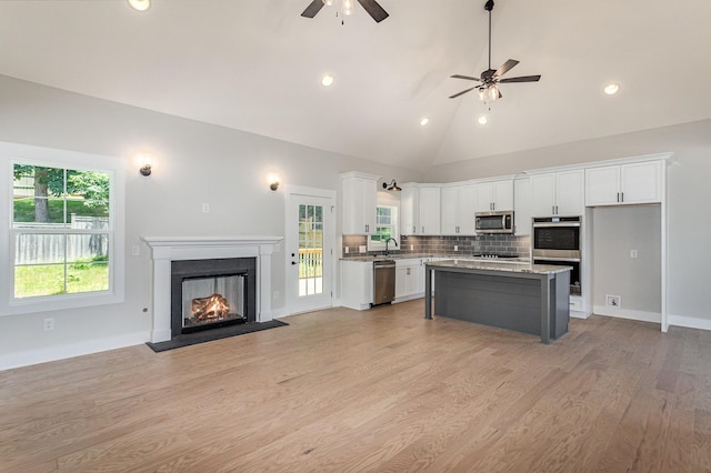 kitchen with a kitchen island, white cabinets, light hardwood / wood-style floors, stainless steel appliances, and light stone countertops