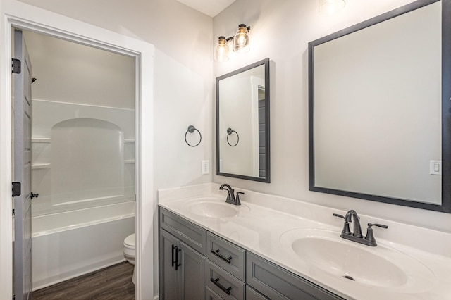 bathroom featuring toilet, double vanity, a sink, and wood finished floors