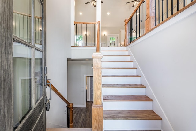 staircase with a high ceiling, wood-type flooring, and ceiling fan