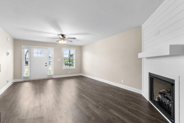 unfurnished living room featuring dark hardwood / wood-style floors, a large fireplace, and ceiling fan