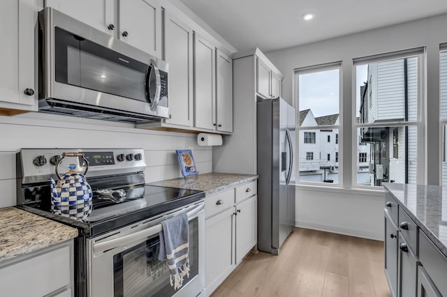 kitchen with light stone counters, white cabinetry, stainless steel appliances, and light wood-type flooring