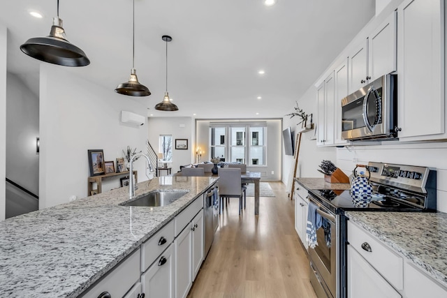 kitchen with sink, white cabinets, hanging light fixtures, light hardwood / wood-style floors, and stainless steel appliances