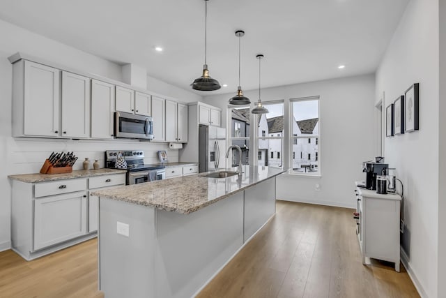 kitchen with appliances with stainless steel finishes, decorative light fixtures, sink, a kitchen island with sink, and light stone counters